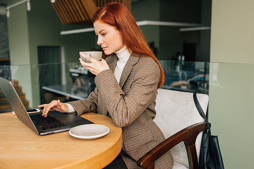 Businesswoman in formal wear typing on laptop in cafe. Young female drinks coffee and work remotely.