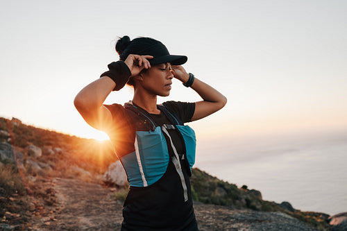 Trail runner taking a break. Woman holding her hat during hike at sunset.