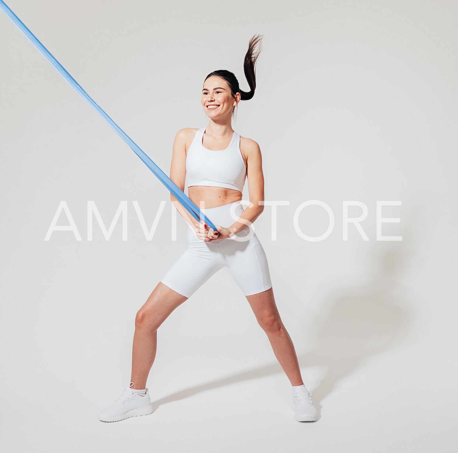 Full length of a slim woman in white fitness wear practicing with a resistance band in a studio