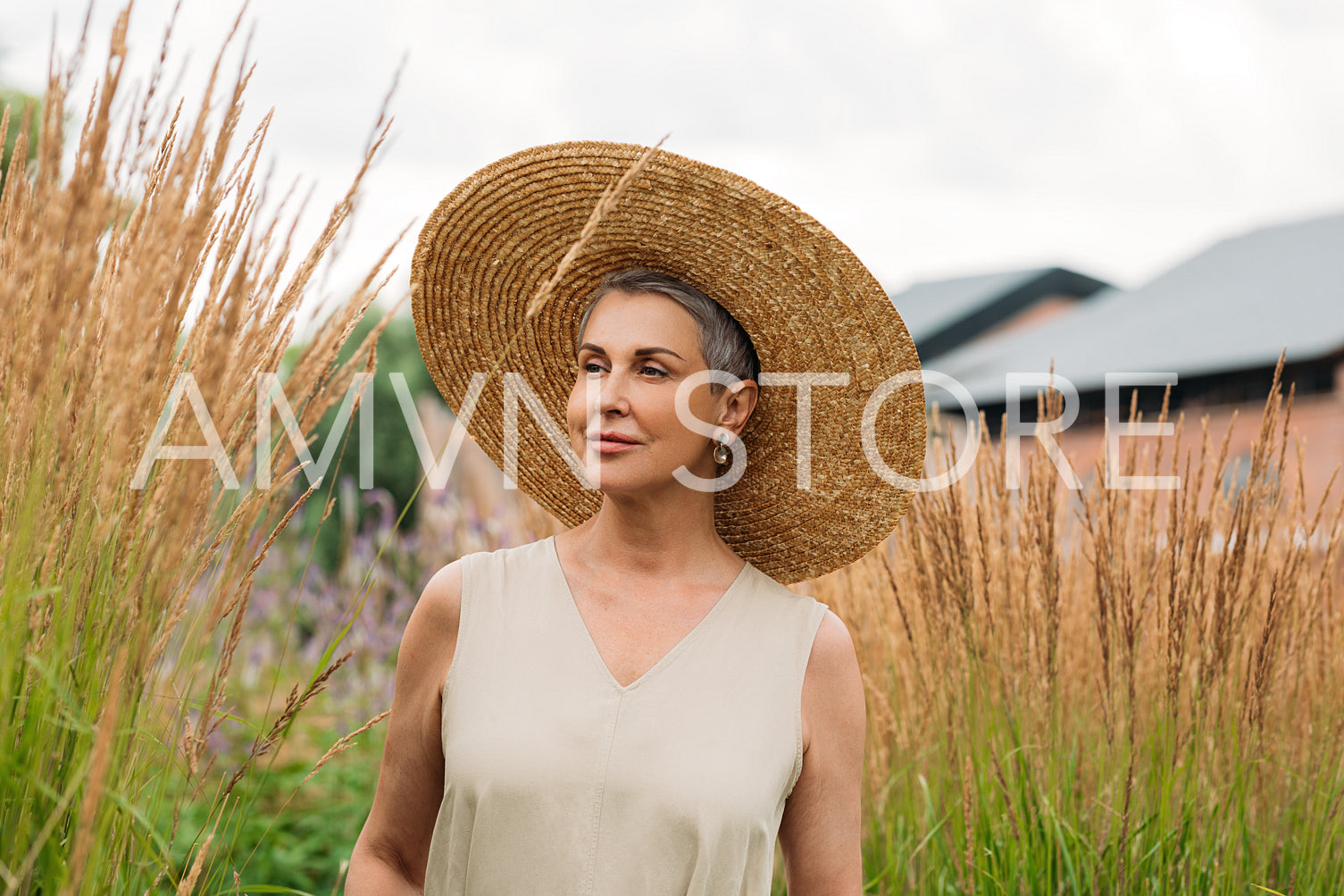 Aged woman with grey hair wearing a big straw hat walking on the wheat field