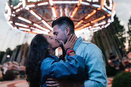 Young couple kissing in an amusement park at the evening