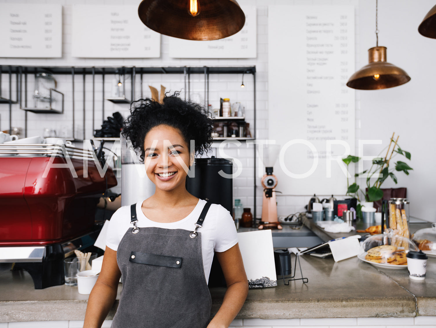 Young smiling barista wearing apron, standing at cafe counter	