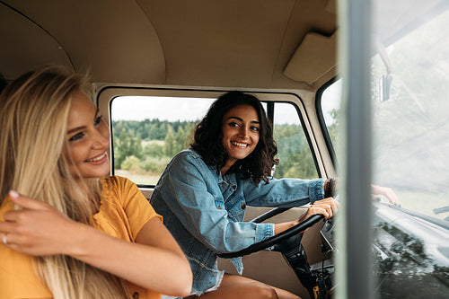 Young woman sitting on a driver seat in camper van. Two women in a car during a road trip.