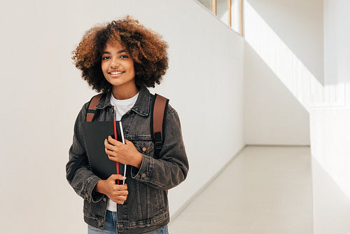 Young woman with curly hair standing in college corridor and looking at camera