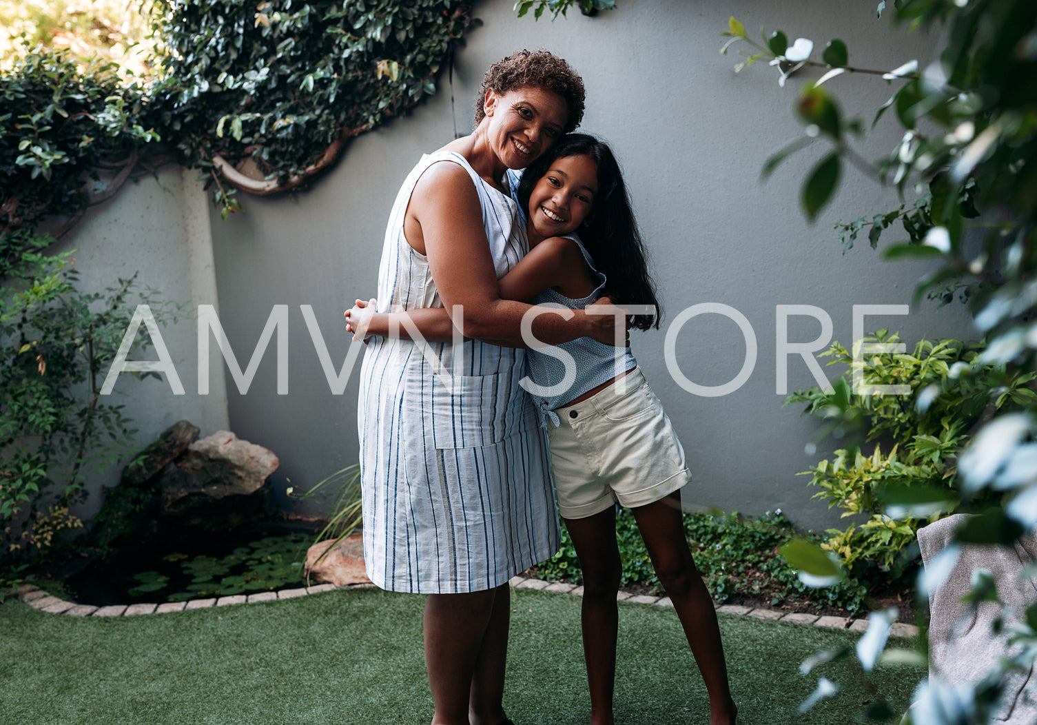 Smiling grandma and her granddaughter embrace while standing outdoors in the backyard