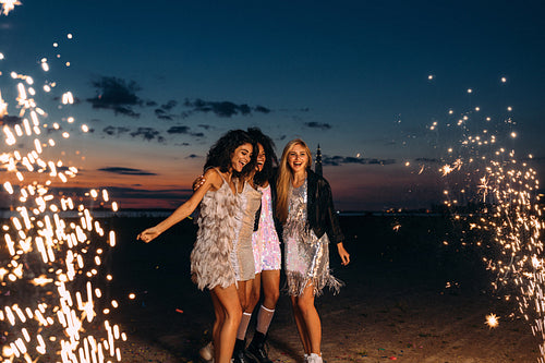 Four beautiful women standing outdoors between fireworks. Happy friends celebrating at sunset.