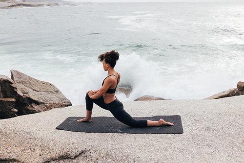 Slim woman stretching her legs on yoga mat. Female practicing yoga by ocean.