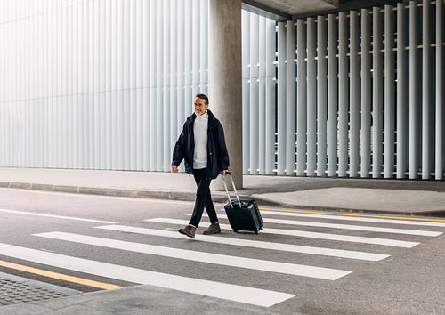 Senior man walking outside public transport building with suitcase