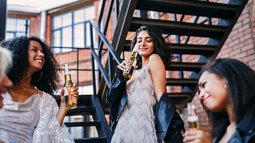 Young woman drinking beer from bottle surrounding by friends outdoors