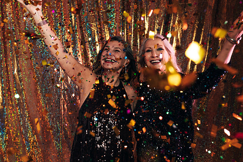 Two happy senior women in black dresses having fun under colorfu