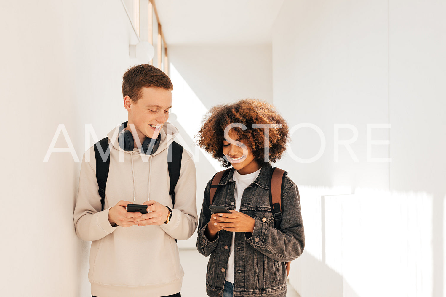 Classmates walking in corridor. Boy and girl in school and looking on their smartphones.