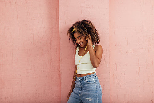 Smiling female enjoying music while standing against wall