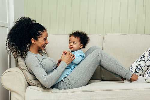 Side view of mother lying on couch and playing with her son