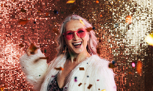 Laughing woman in white fur coat throwing confetti in studio aga