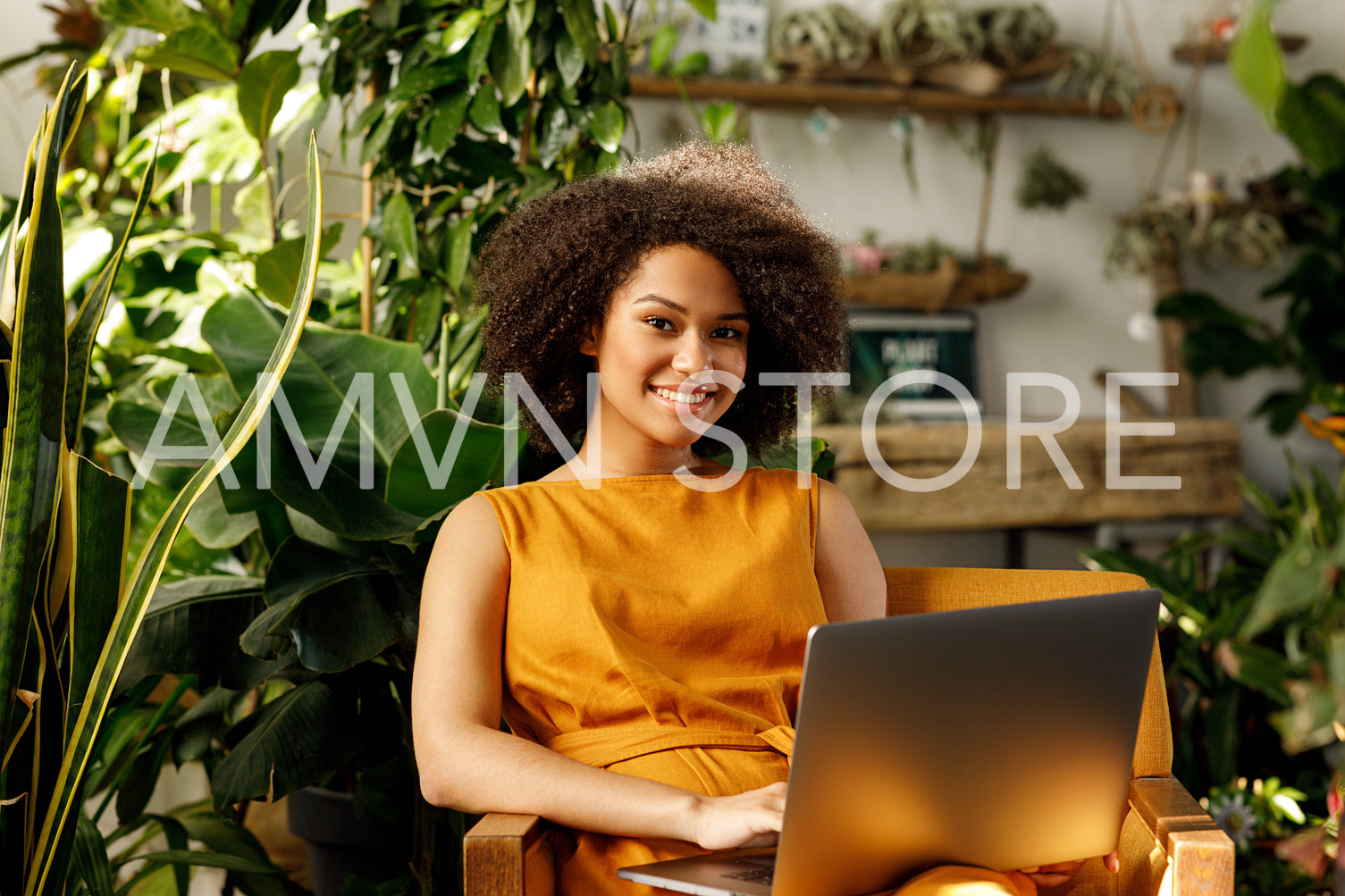 Smiling female florist sitting at her workshop and typing on laptop	