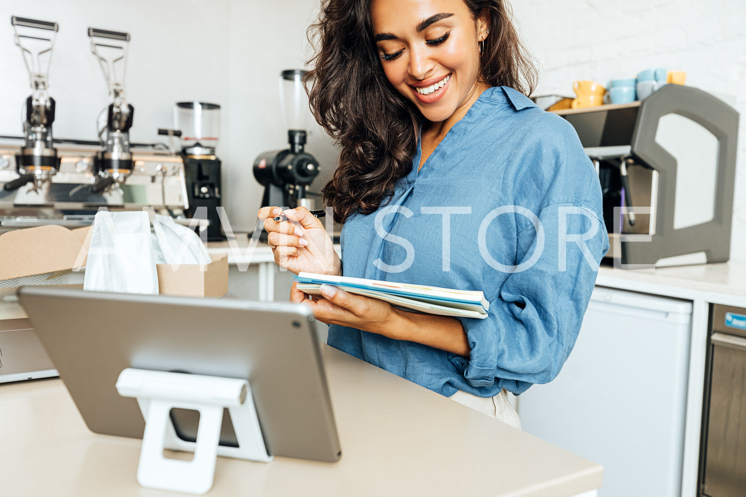 Smiling woman holding a note book in coffee shop. Cafe owner standing at table.	