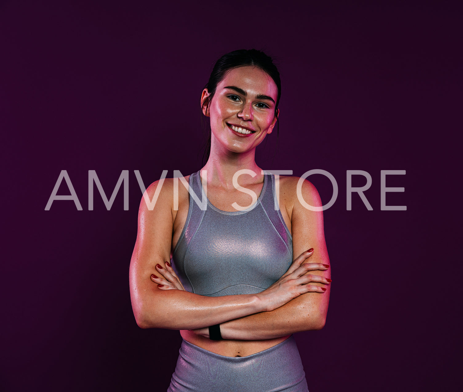 Smiling sportswoman with crossed arms wearing silver sportswear looking at the camera against a magenta background