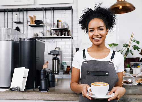 Young smiling woman standing in cafeteria with cup of latte