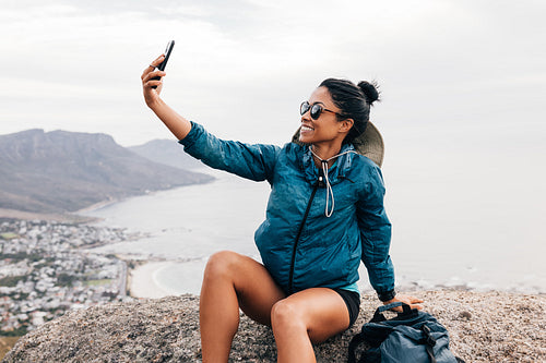 Side view of female hiker taking a selfie and smiling while sitting on a rock