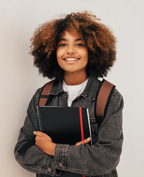 Cheerful girl with curly hair holding a books wearing backpack