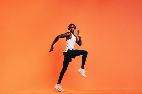 Young athlete in wireless headphones doing intense workout in studio over orange background