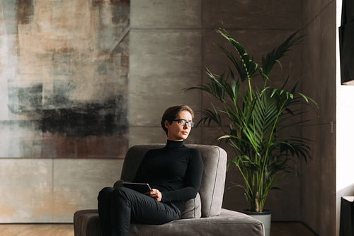 Middle-aged woman in black formal wear wearing glasses holding a digital tablet