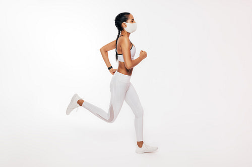 Side view of young fitness woman running over white background wearing a face mask