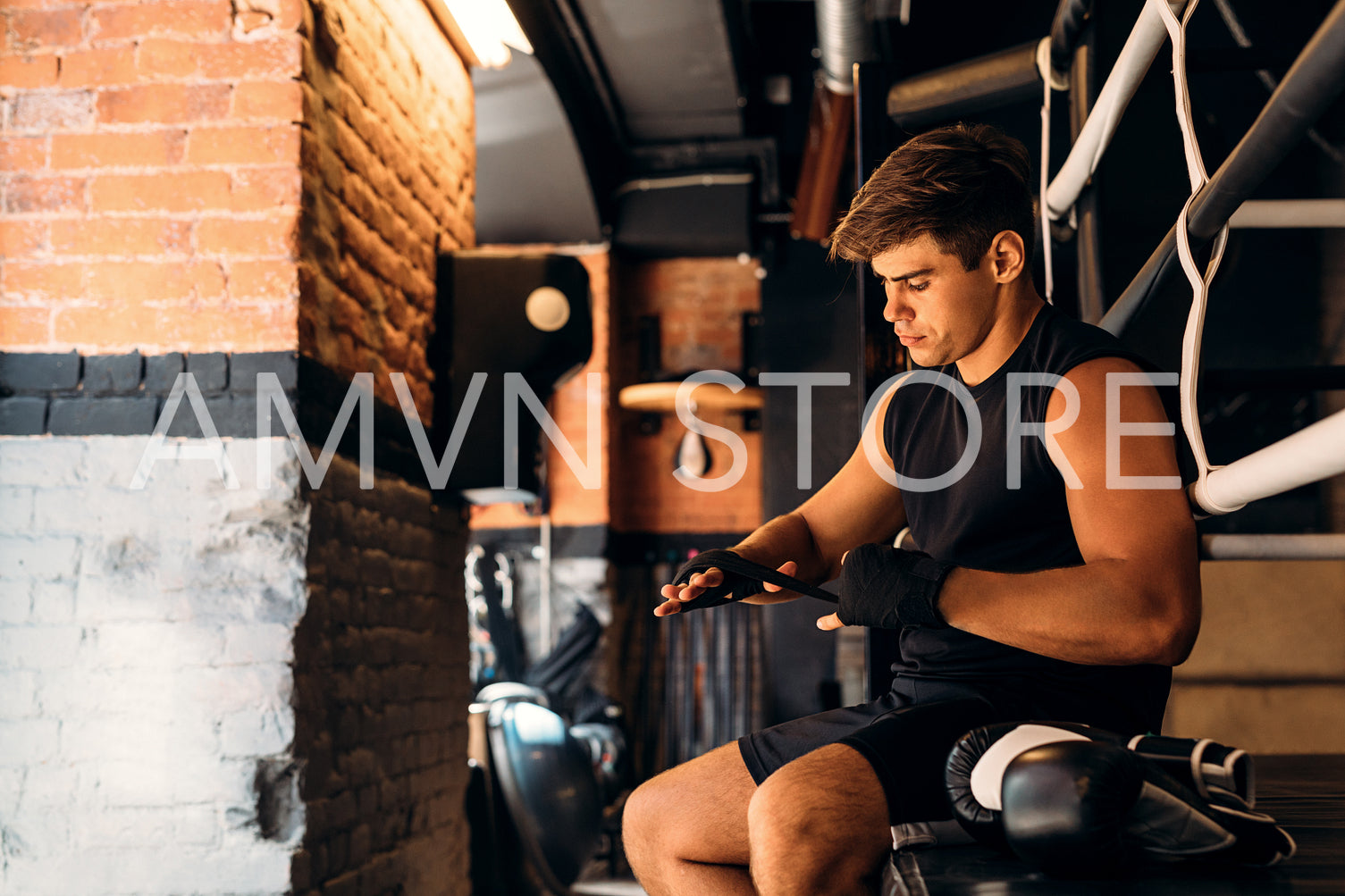 Side view of male boxer wrapping hand with bandage in gym	