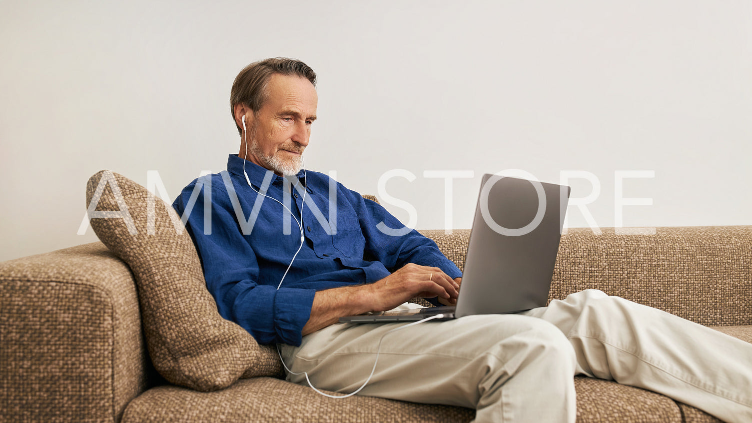 Senior man lying on a couch in the living room with a laptop on his hips