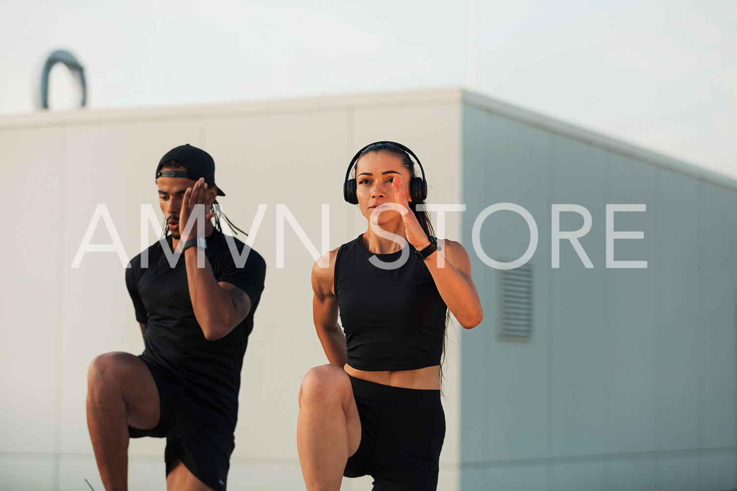 Two athletes doing warming-up exercises on a roof at sunset. Man and woman doing high-intensity exercises together.