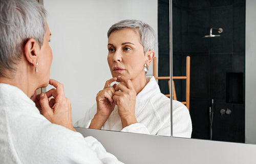 Senior woman spending time at home standing in bathroom looking in a mirror