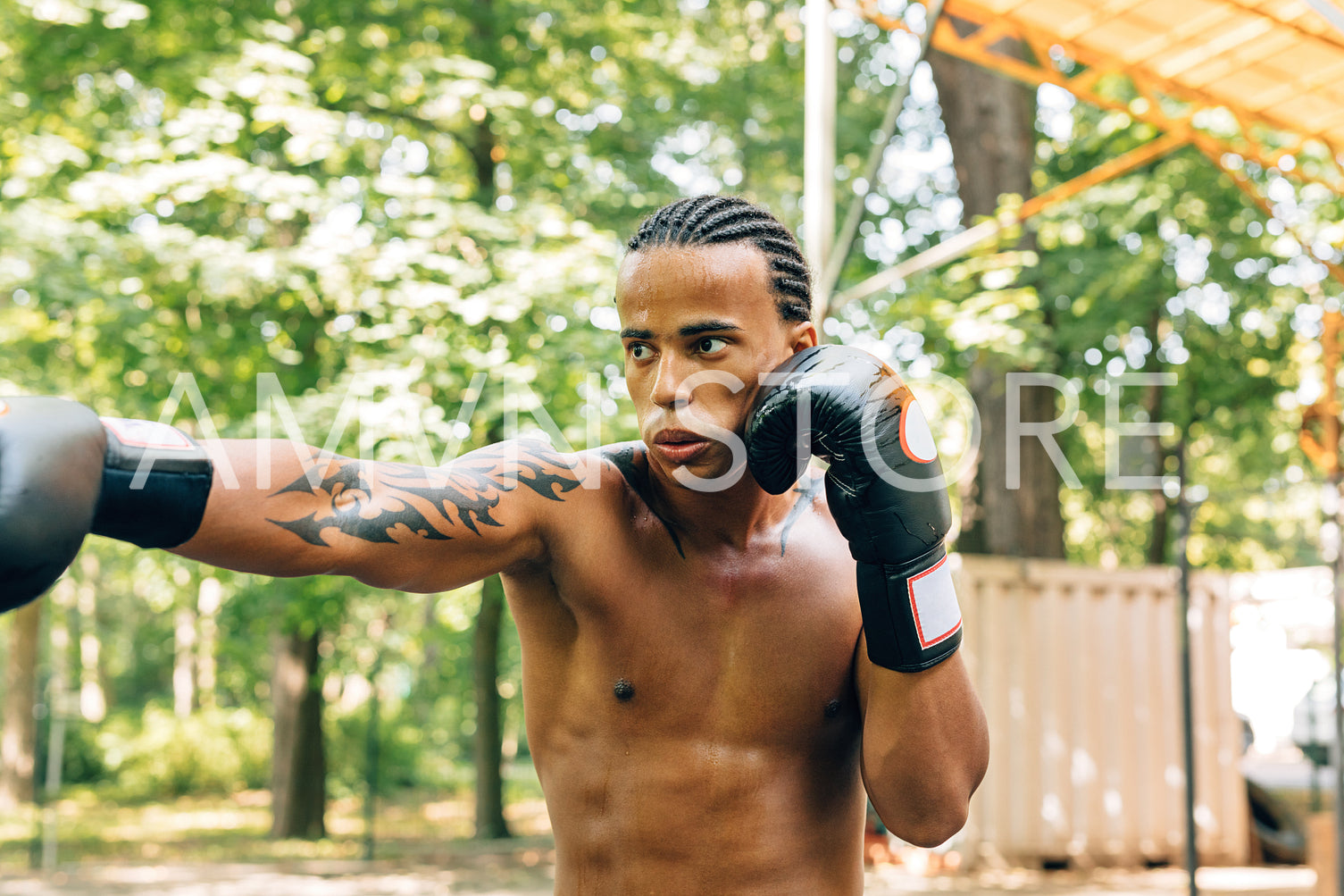 Sweated bare-chested sportsman with boxing gloves exercising outdoors	