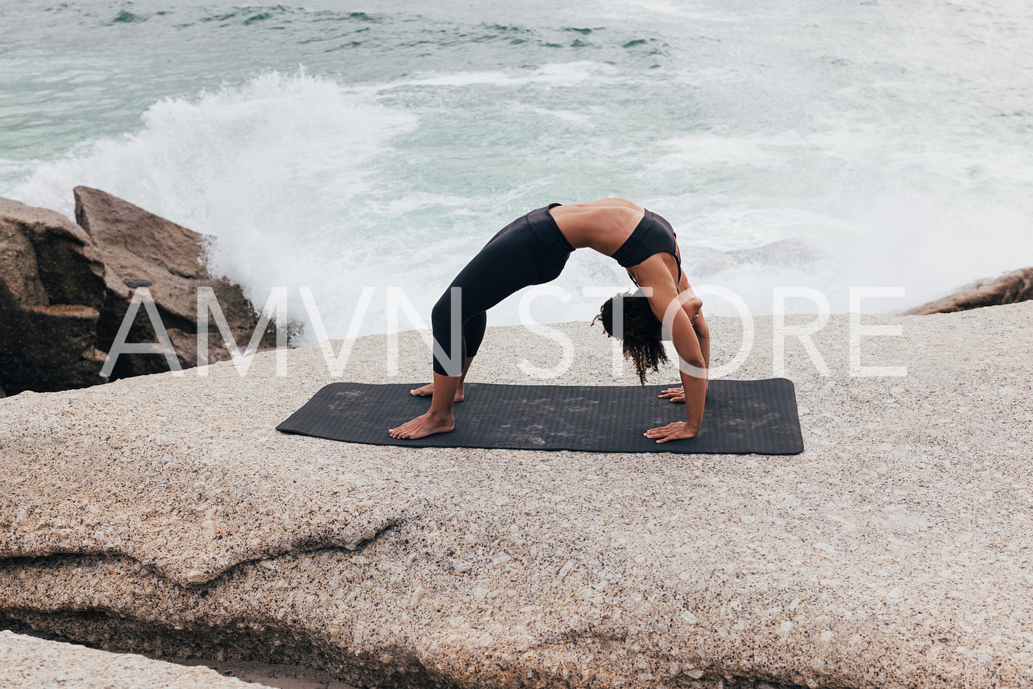 Side view of young slim female practicing Urdhva Dhanurasana. Woman in sportswear in Wheel yoga pose by ocean.