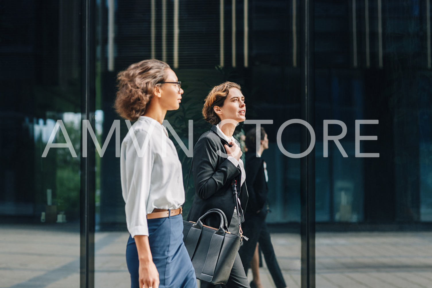 Two businesswomen walking to the office carrying her bags and talking	