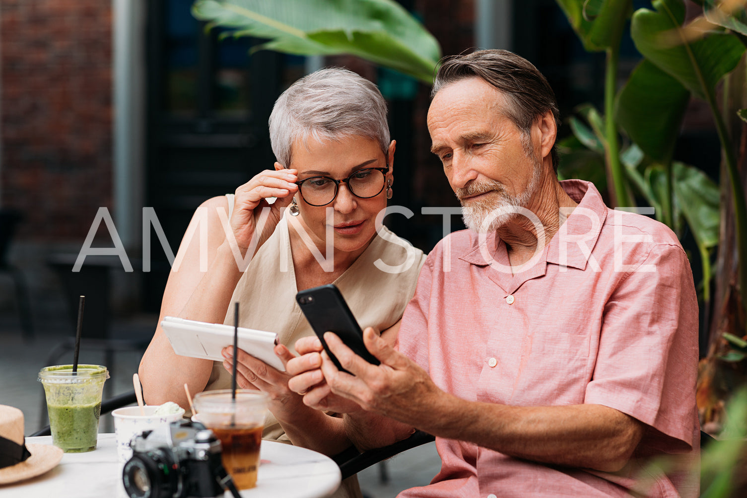 Aged woman looking at her husband's smartphone in an outdoor cafe. Senior man showing his wife something on his smartphone.