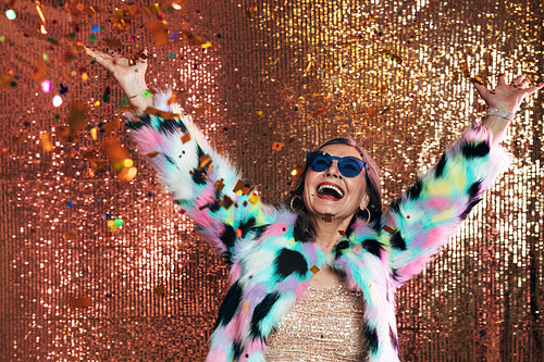 Happy senior woman raising hands up while having fun under confe