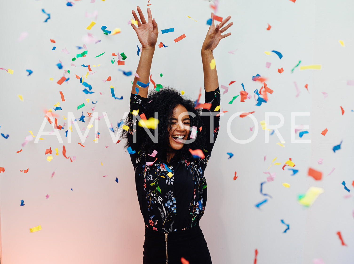 Young beautiful woman laughing under colorful confetti, raised her hands up	