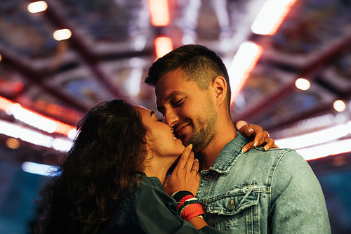 Young romantic couple against night lights in an amusement park