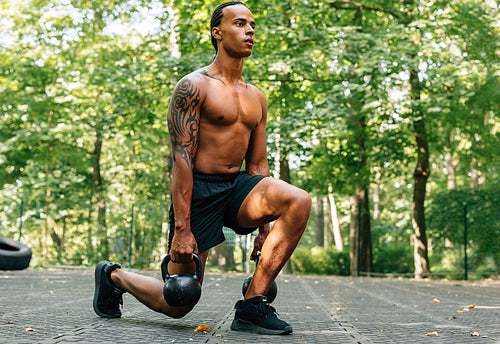 Man exercising with kettlebell outdoors. Athlete doing squats using kettlebells.