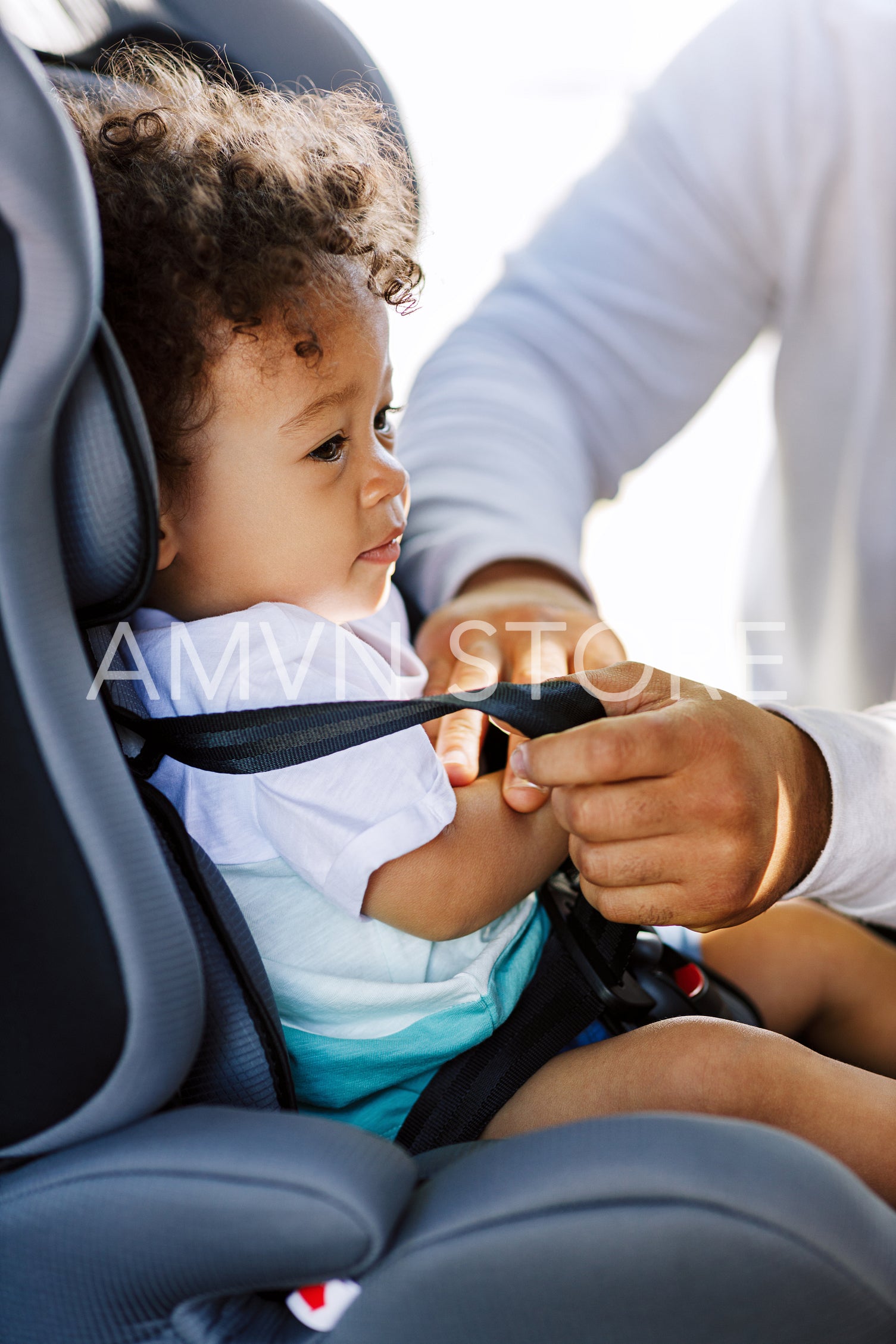 Side view of a little boy in the car seat. Hands of man buckling seat straps.	