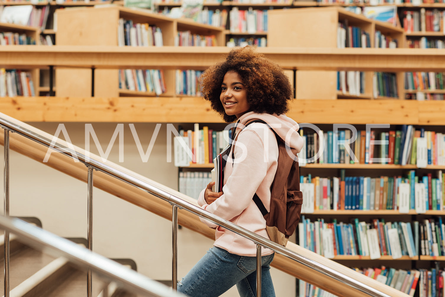 Smiling girl walking on stairs in library. Student in college library.