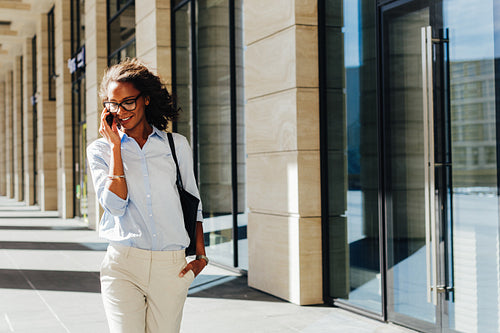 Woman walking at office building. Young entrepreneur talking on cell phone.