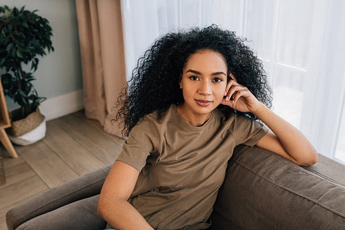 Portrait of a beautiful woman with black curly hair sitting on couch in living room