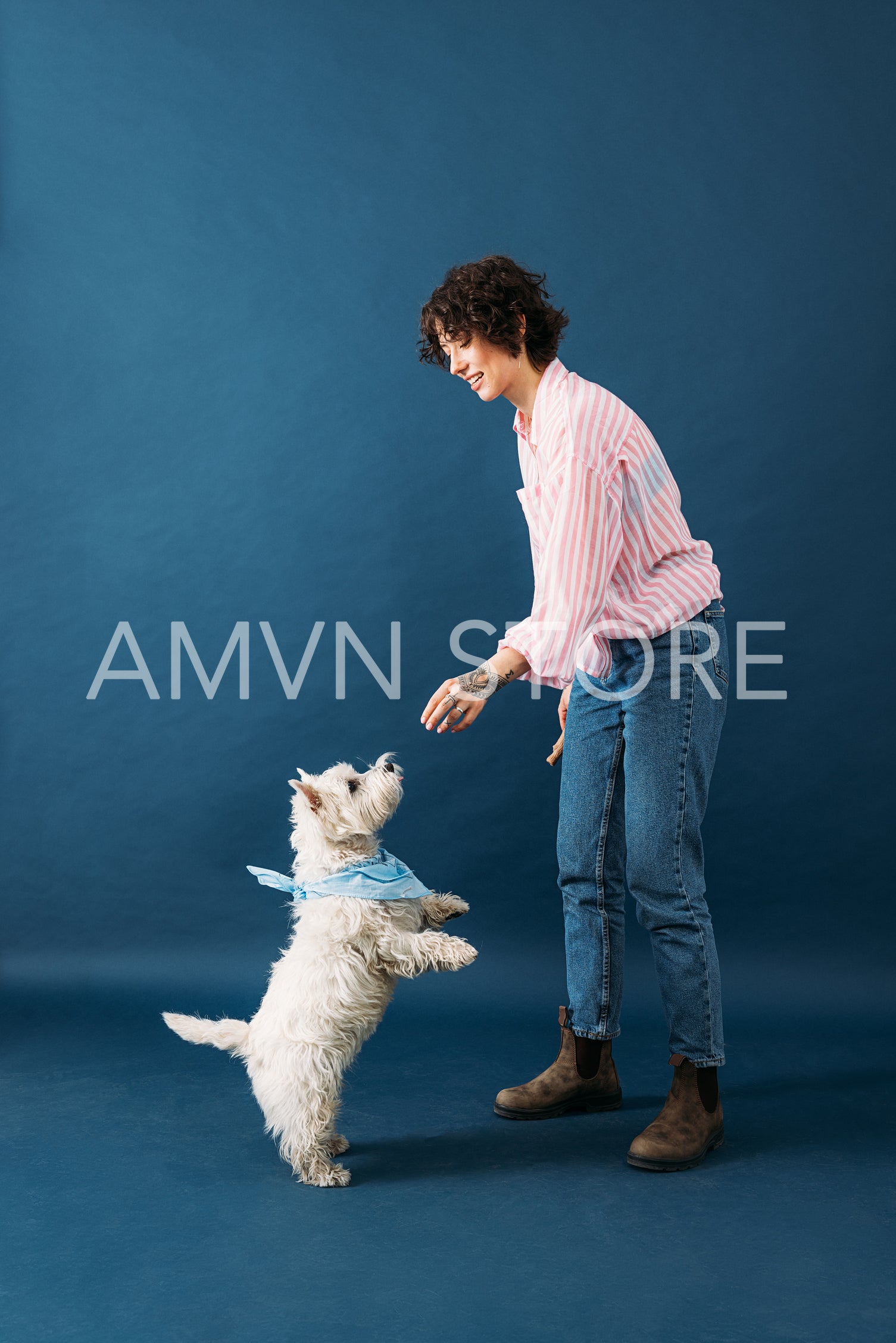 Side view of young woman in casuals standing in studio on blue b