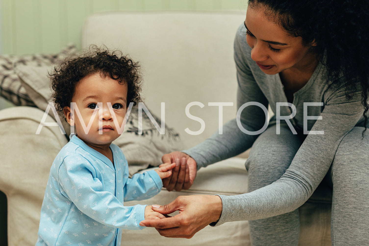 Young mother holding her child hands in living room. Toddler looking at camera.	