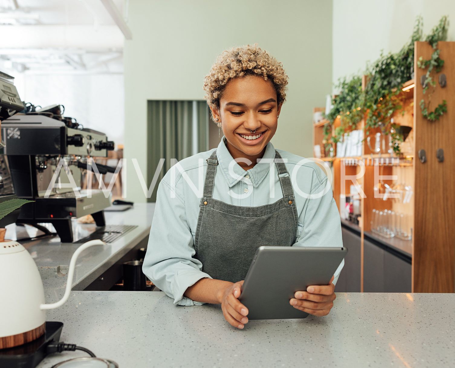 Young smiling barista holding a digital tablet at bar counter. Female entrepreneur in an apron with digital tablet in her cafe.