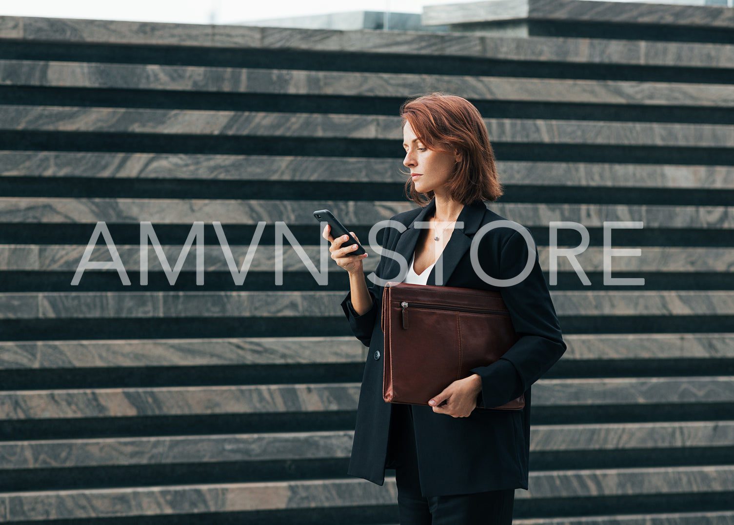 Side view of middle-aged businesswoman with leather folder and smartphone walking outdoors