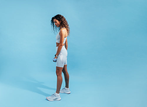 Fit woman posing on blue background. Side view of young sports woman relaxing.