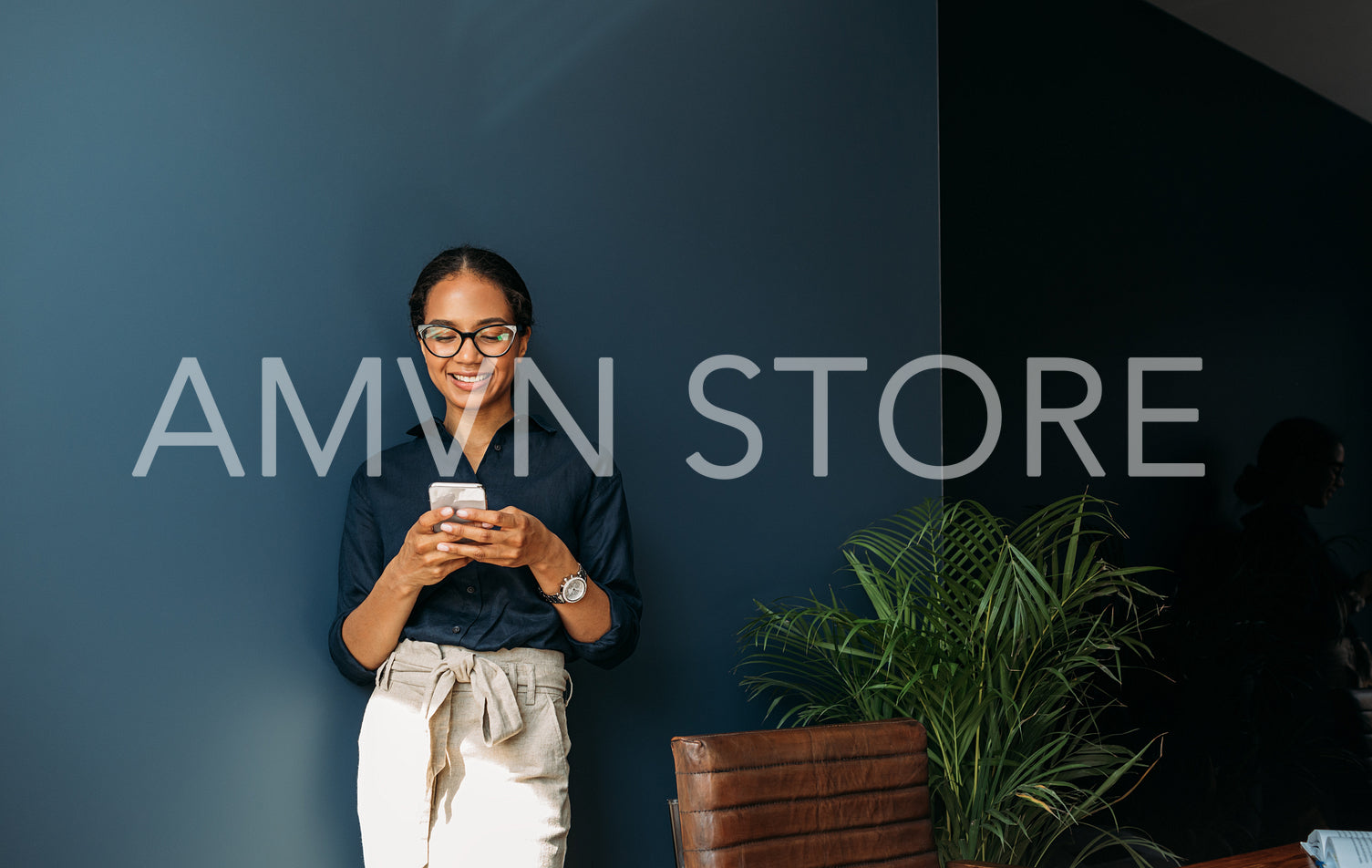 Smiling businesswoman typing on cell phone at the blue wall