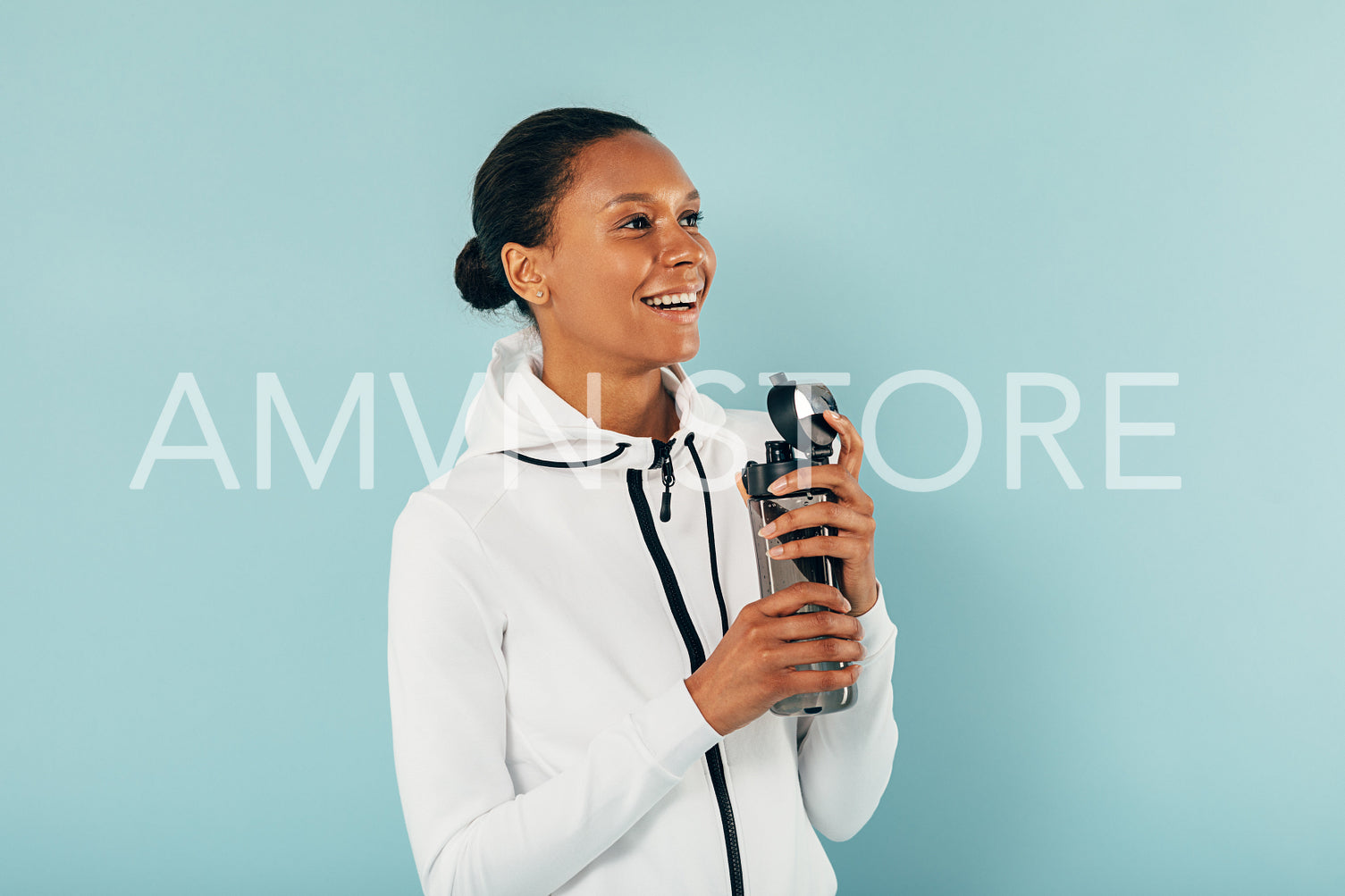 Happy woman in sports clothes holds a water bottle and looking away in studio over blue background	